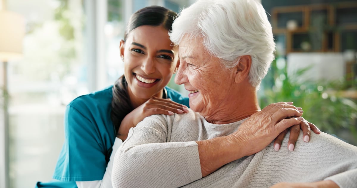 African American nurse smiling with elderly African American woman in retirement home living room